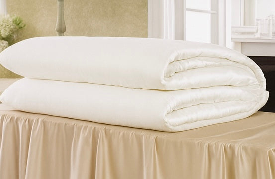 A white silk duvet from Athena folded on a table. The luxury duvet is filled with mulberry silk filling and has a 100 percent long staple cotton shell. 