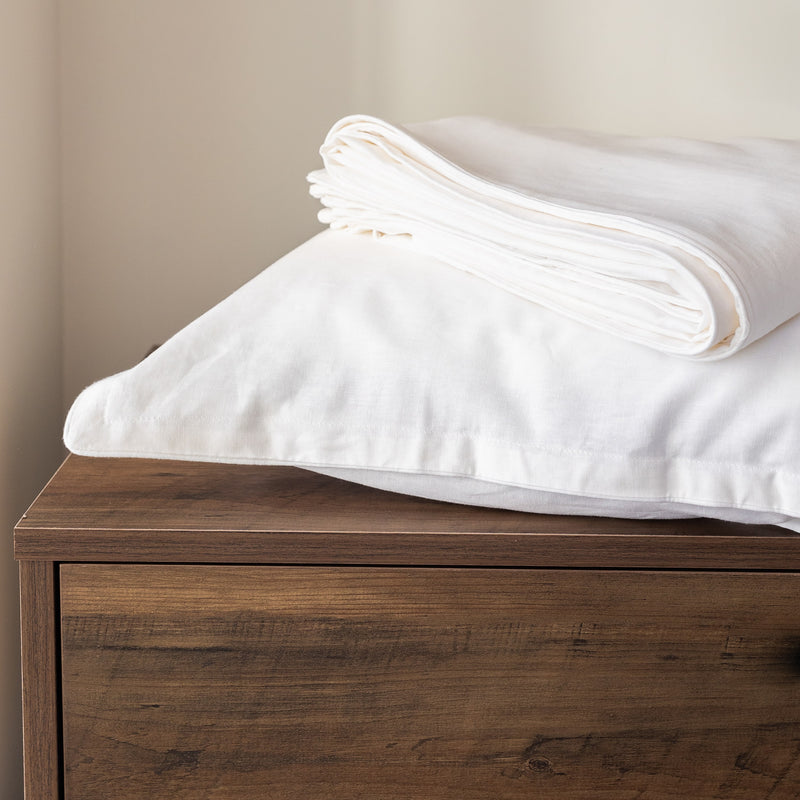 Folded white comforter on a wooden dresser against a beige wall from Hometrend, a canadian bedding company.